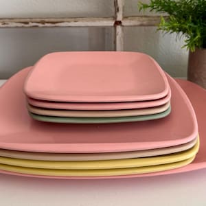 May include: A stack of square, pastel-colored plates. The plates are in shades of pink, yellow, and green. The plates are stacked on top of each other, with the largest plate at the bottom and the smallest at the top. The plates have rounded corners.