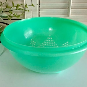 May include: A bright green plastic colander bowl with a wide rim and small drainage holes. The bowl is empty and sits on a white surface. The colander is designed for washing and draining fruits and vegetables.