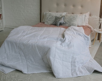 May include: A white quilted bedspread with a pink throw pillow and a white headboard with tufted buttons. The bed is in a bedroom with a white brick wall and a white shelf with books.