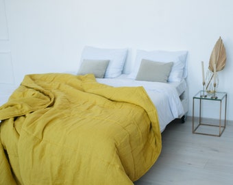Könnte beinhalten: Ein Bettkissenbezug aus gelbem Leinen bedeckt ein weißes Bett mit zwei weißen Kissen und zwei beigen Kissen. Ein kleiner Glas-Beistelltisch mit goldenem Metallrahmen steht neben dem Bett.