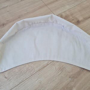 May include: A white fabric cushion with a curved shape. The cushion is made of a soft, smooth fabric and has a simple design.