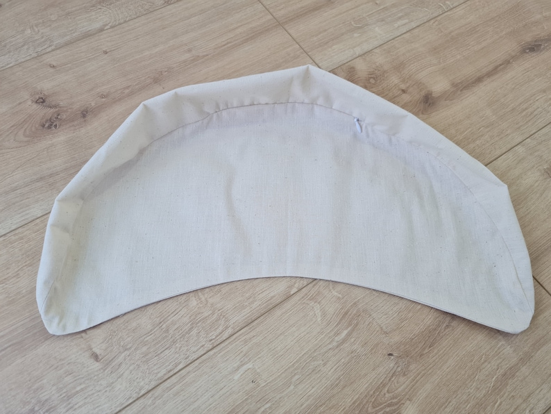 May include: A white fabric cushion with a curved shape. The cushion is made of a soft, smooth fabric and has a simple design.