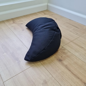 May include: A solid dark navy blue crescent-shaped pillow with a smooth fabric exterior. The pillow features a curved, moon-like silhouette with stitched seams along the edges, providing a structured form that rests on its side on the floor.