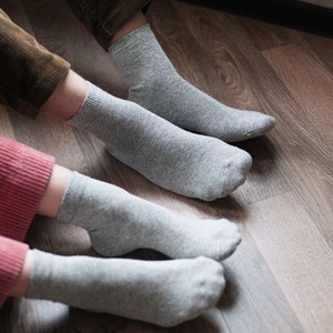 May include: Two pairs of gray socks on a wooden floor. The socks are made of a soft, comfortable material and are perfect for everyday wear.