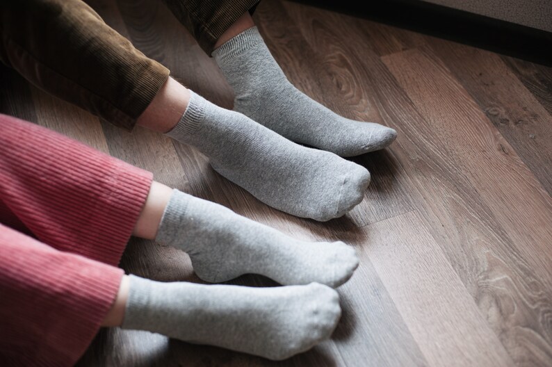May include: Two pairs of gray socks on a wooden floor. The socks are made of a soft, comfortable material and are perfect for everyday wear.