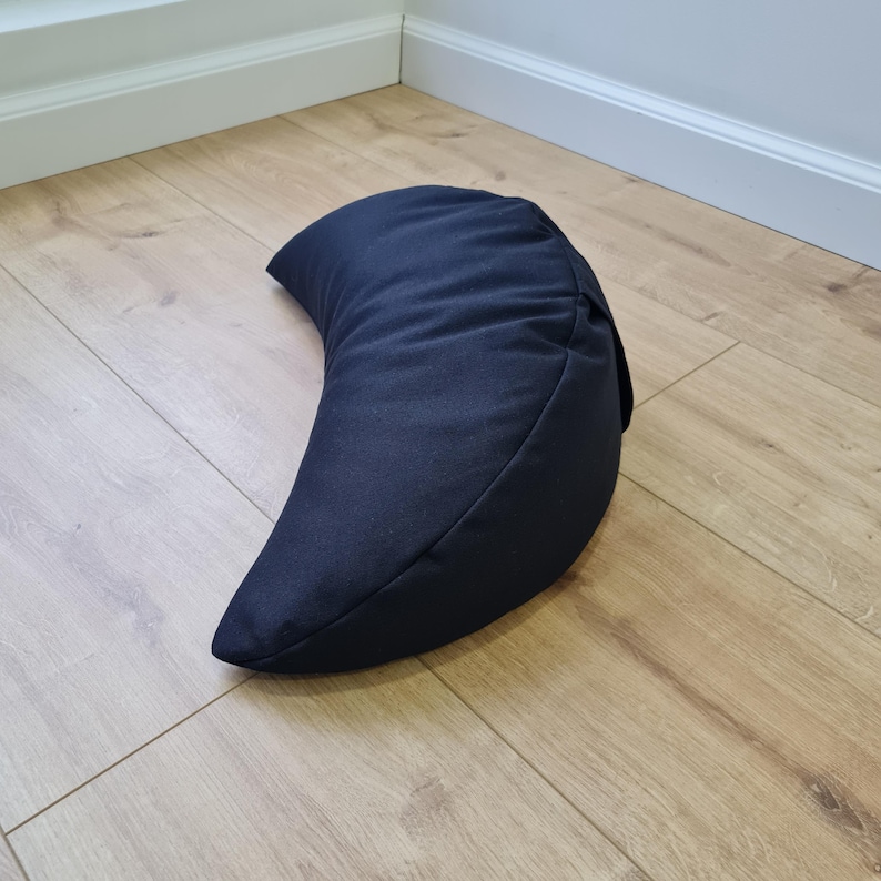 May include: A solid dark navy blue crescent-shaped meditation cushion. The pillow features a smooth, matte fabric exterior with a curved, ergonomic design that tapers to pointed ends, providing a firm and structured form for seated support.