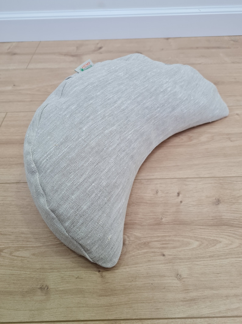 May include: A crescent-shaped meditation cushion made of gray hemp fabric. The cushion has a label that says "HEMP" with a green leaf logo.
