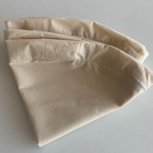 May include: A folded beige fabric tablecloth, with a smooth texture and a slightly curved shape.