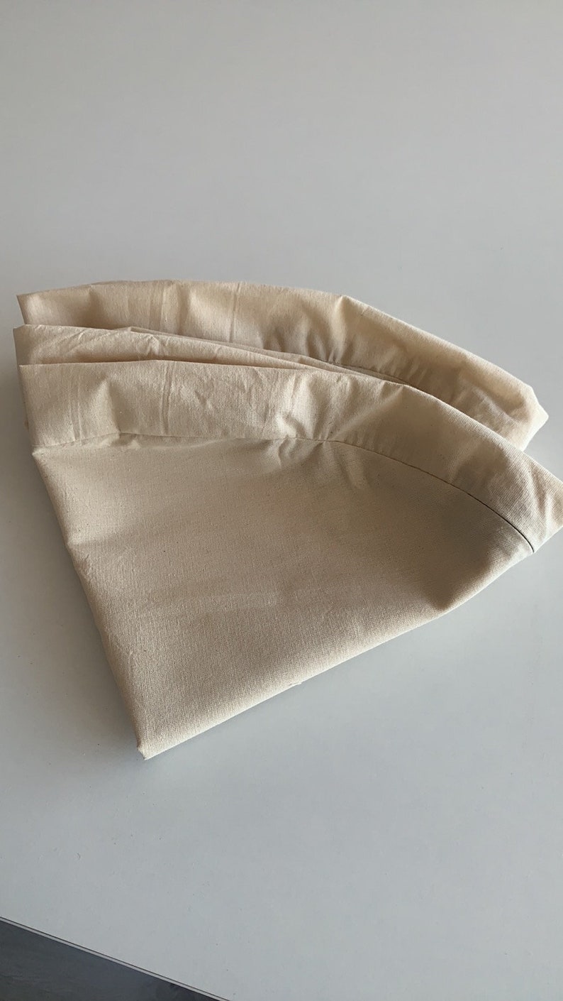 May include: A folded beige fabric tablecloth, with a smooth texture and a slightly curved shape.