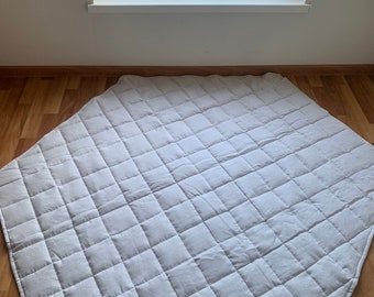 Könnte beinhalten: Eine weiße, gesteppte, sechseckige Spielmatte mit Rautenmuster. Die Matte liegt auf einem Holzboden.