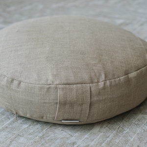 May include: A round, beige linen meditation cushion. The cushion is filled with a soft, comfortable material and is perfect for sitting on the floor.
