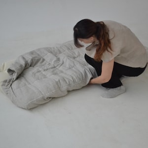 May include: A person is folding a grey and white quilted cushion. The cushion is made of a soft, textured fabric and has a simple, modern design.