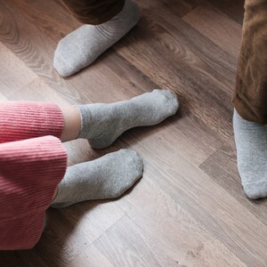 May include: Two pairs of grey socks on a wooden floor. One pair is on a person's feet, the other pair is on the floor.