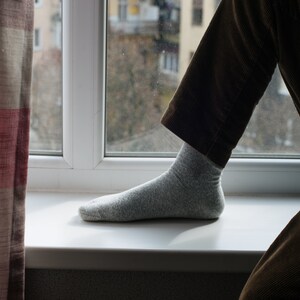 May include: A person's foot wearing a gray sock, resting on a white windowsill. The person is wearing brown corduroy pants.