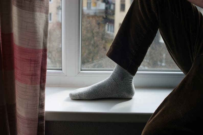 May include: A person's foot wearing a gray sock, resting on a white windowsill. The person is wearing brown corduroy pants.