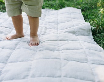 Könnte beinhalten: Die nackten Füße eines Kindes stehen auf einer weißen gesteppten Decke. Die Decke liegt auf einer grasbewachsenen Fläche.