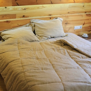 May include: A bed with a beige duvet cover and a wooden headboard. The bed is made with beige pillows and a beige blanket. There is a small wooden bedside table next to the bed.