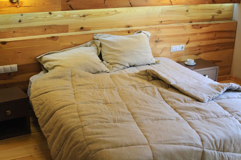 May include: A bed with a beige duvet cover and a wooden headboard. The bed is made with beige pillows and a beige blanket. There is a small wooden bedside table next to the bed.