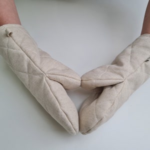 May include: A pair of beige quilted oven mitts with a loop on each for hanging.