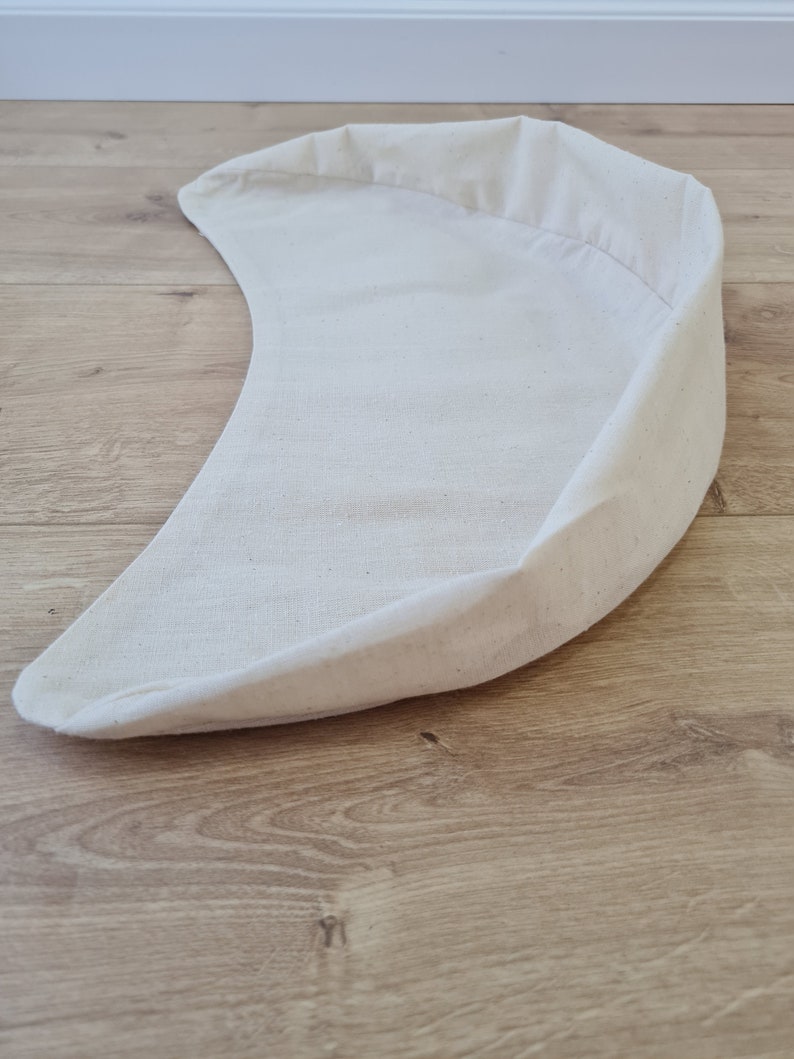 May include: A white crescent-shaped fabric cushion, ideal for a pet bed or a decorative accent.