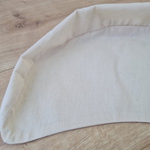 May include: A white fabric cushion with a curved shape and a sewn edge.