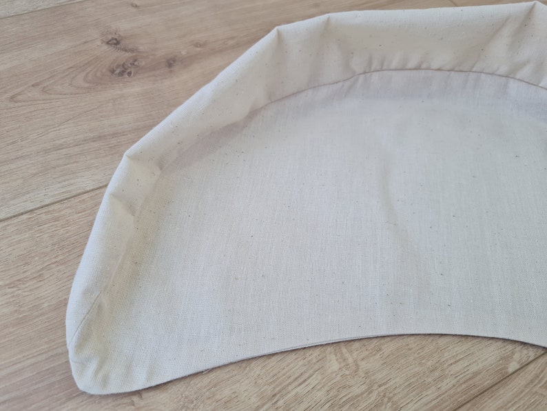 May include: A white fabric cushion with a curved shape and a sewn edge.