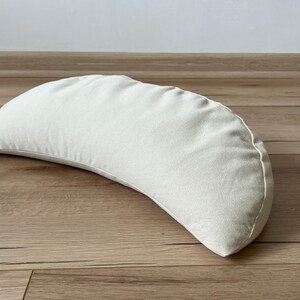 May include: A white crescent-shaped meditation cushion made of fabric.