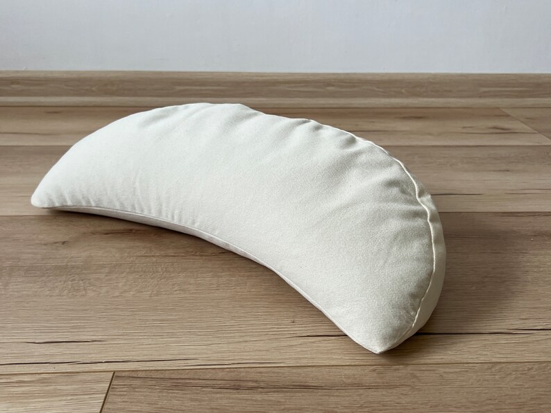 May include: A white crescent-shaped meditation cushion made of fabric.