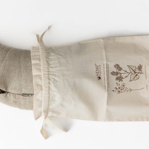May include: A beige hemp pillow filled with buckwheat hulls, in a natural cotton drawstring bag. The bag has a label that reads "HEMP* ORGANIC LIFE" and features illustrations of hemp and flax plants.