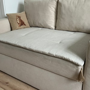 May include: A beige sofa with a striped cushion with tassels. The cushion has a light gray and white striped pattern.