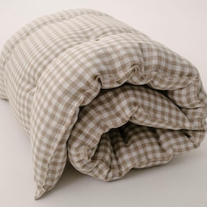 May include: A rolled up beige and white gingham patterned baby crib mattress.