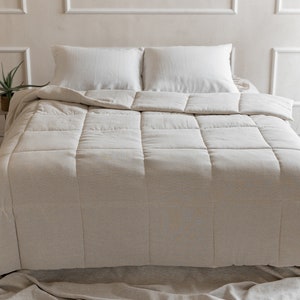 May include: A white linen duvet cover with a quilted design. The duvet is on a bed with white linen pillowcases.