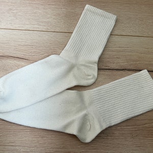 以下が含まれることがあります： リブのついた白い綿の靴下2足。靴下は半分に折り畳まれ、木製の表面に平らに置かれています