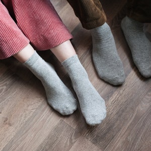 May include: Two pairs of grey socks on a wooden floor. One pair is on a person's feet, the other pair is on the floor.