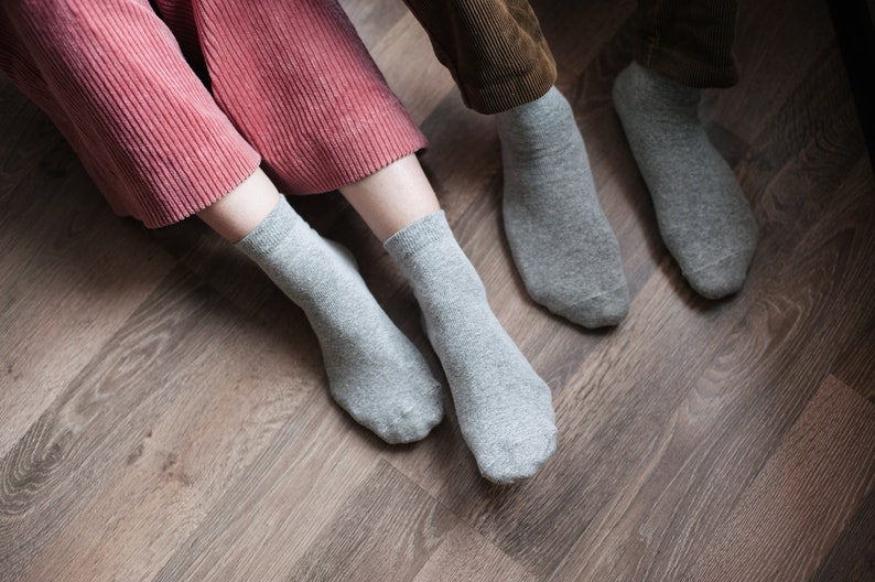 May include: Two pairs of grey socks on a wooden floor. One pair is on a person's feet, the other pair is on the floor.