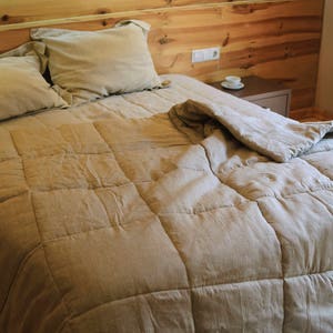 May include: A beige linen duvet cover with a quilted pattern, on a bed with two pillows. The bed is made with a wooden headboard and is in a bedroom setting.