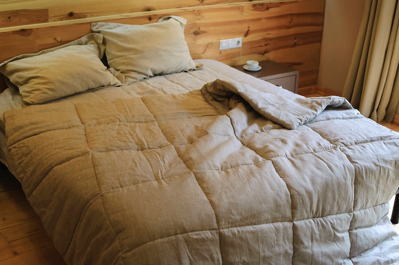 May include: A beige linen duvet cover with a quilted pattern, on a bed with two pillows. The bed is made with a wooden headboard and is in a bedroom setting.