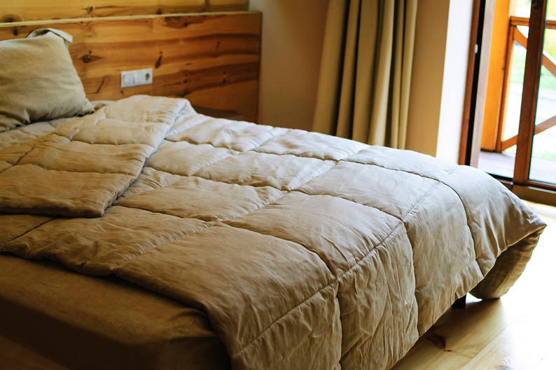 May include: A close-up of a beige duvet with a quilted pattern, lying on a bed with a wooden headboard. The duvet is folded back to reveal the white sheets underneath.