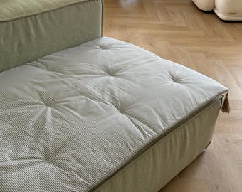 May include: Close-up of a section of a light green sofa with a striped cushion. The cushion has a tufted design with a light gray and white striped pattern. A small tassel hangs from the corner of the sofa.
