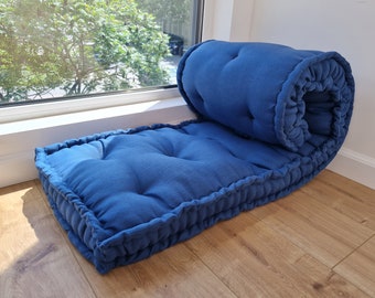 May include: A blue floor cushion with a tufted top and a rolled-up end. The cushion is made of a soft, textured fabric.