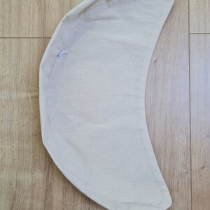 May include: A cream-colored crescent-shaped fabric cushion with a white drawstring.