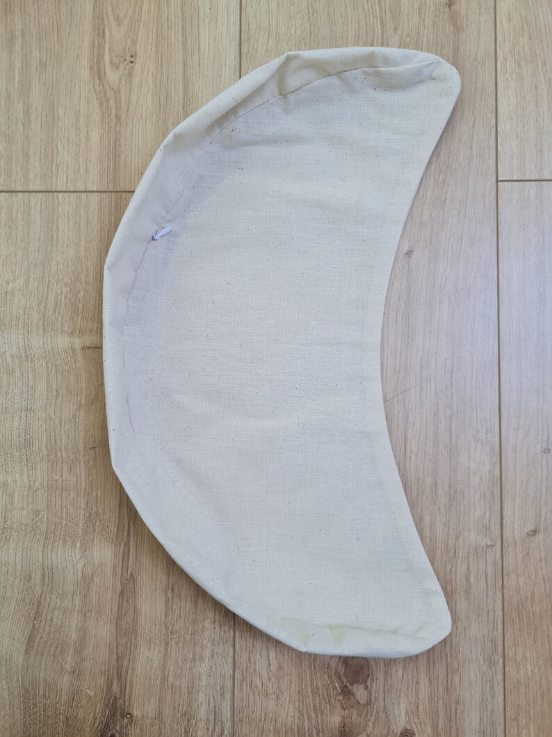 May include: A cream-colored crescent-shaped fabric cushion with a white drawstring.