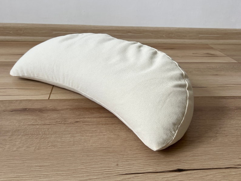 May include: A crescent-shaped, off-white meditation cushion made of fabric.