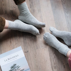 May include: Two pairs of gray socks on a wooden floor. The socks are made of a soft, comfortable material. The socks are a neutral color and can be worn with a variety of outfits.