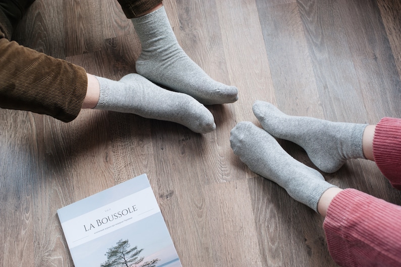 May include: Two pairs of gray socks on a wooden floor. The socks are made of a soft, comfortable material. The socks are a neutral color and can be worn with a variety of outfits.