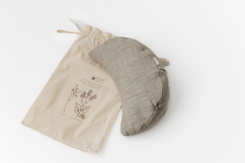 May include: A gray hemp meditation cushion in the shape of a crescent moon, with a hemp drawstring bag. The bag has a printed design of herbs and the text "HEMP ORGANICS".