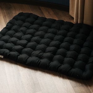 May include: Black floor cushion with a tufted design. The cushion is made of a soft, comfortable fabric and is perfect for sitting on the floor.