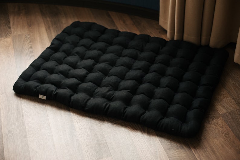 May include: Black floor cushion with a tufted design. The cushion is made of a soft, comfortable fabric and is perfect for sitting on the floor.