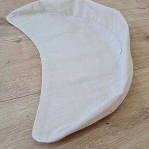 May include: A white cotton crescent-shaped cushion with a zipper closure.