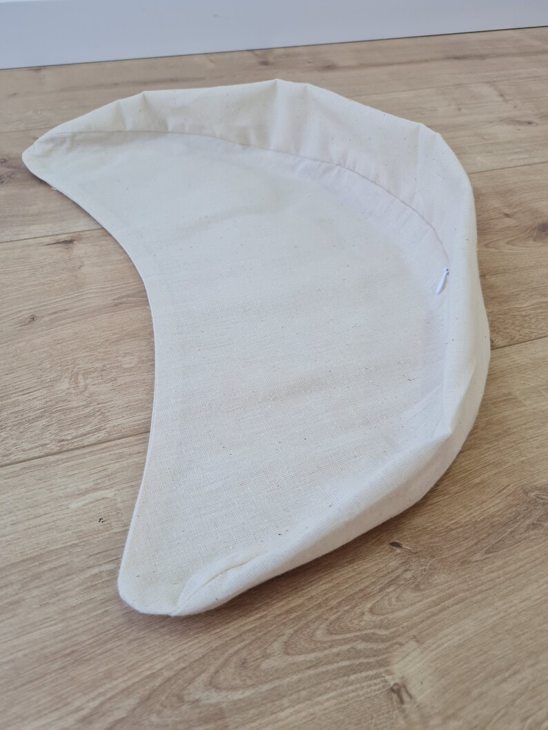 May include: A white cotton crescent-shaped cushion with a zipper closure.